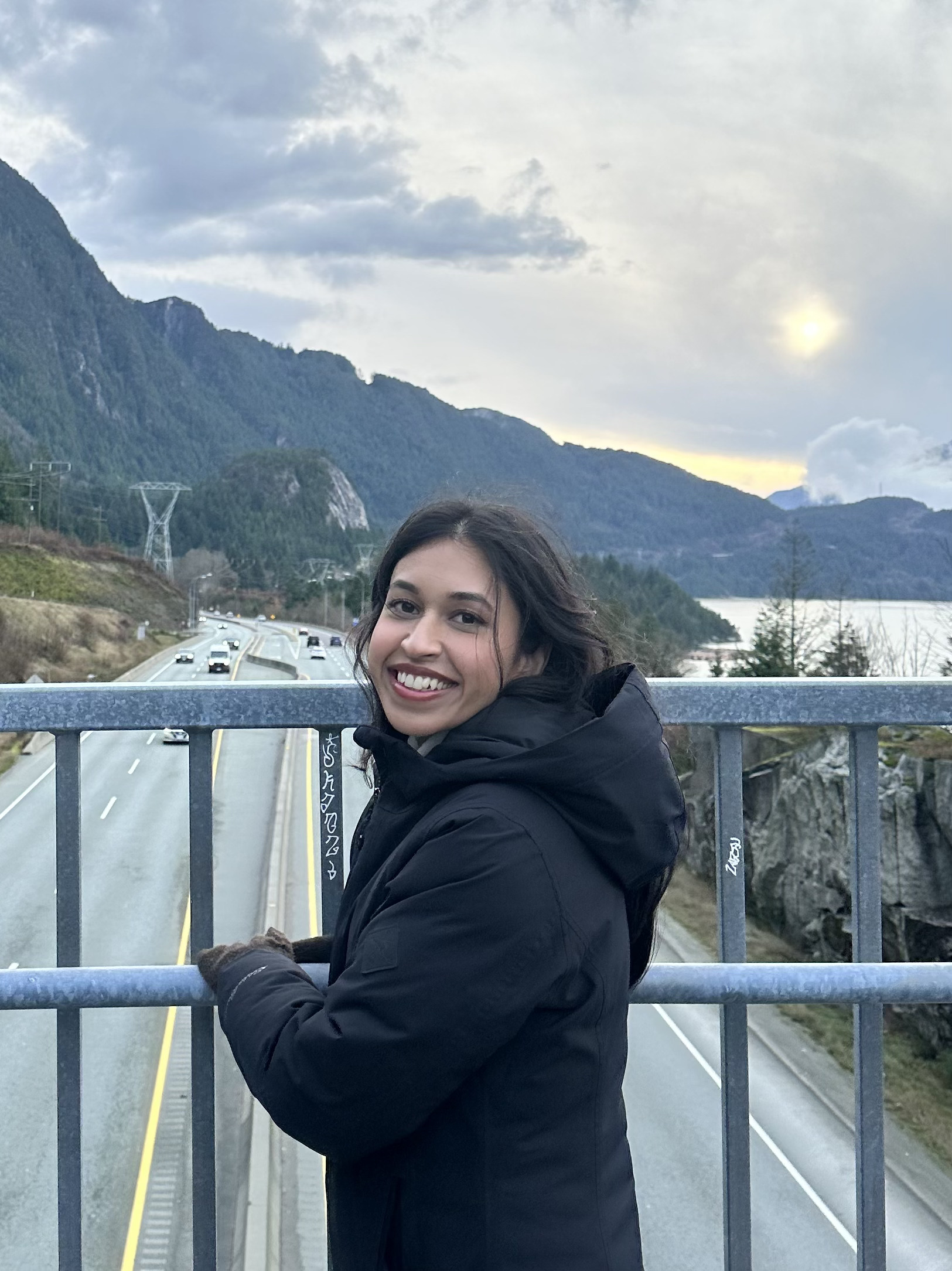 Author smiling at the camera on a bridge with mountains in the background.